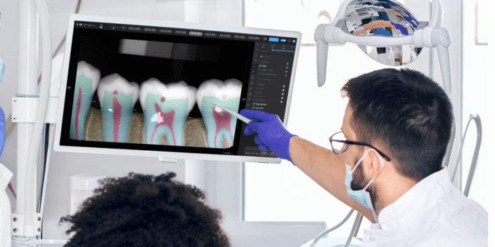 A dentist points at a computer screen featuring images of teeth
