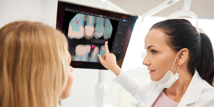 A dentist points at a screen featuring a scan of teeth